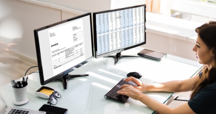 woman typing on a computer while looking at an invoice