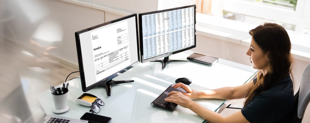 woman typing on a computer while looking at an invoice
