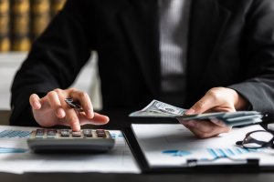 person typing on calculator while holding money