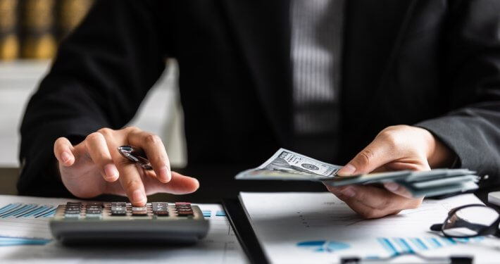 person typing on calculator while holding money