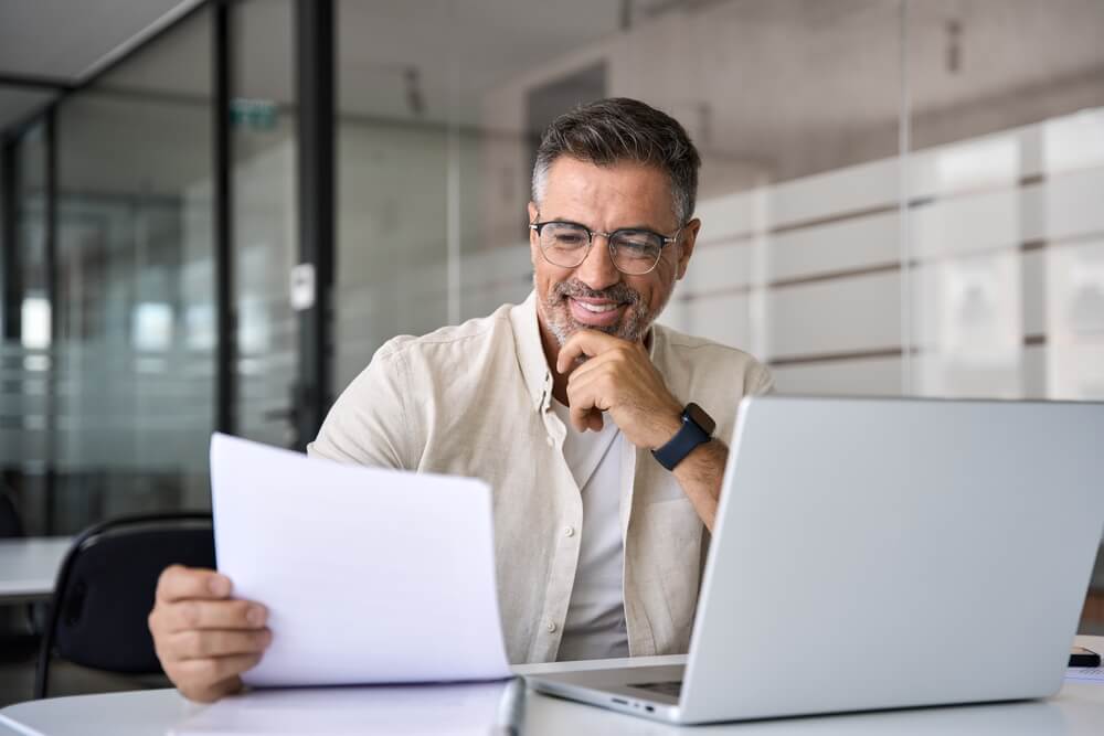 business owner smiling at papers in his hand while sitting at his desk
