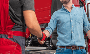 truckers shaking hands in front of red semi-truck