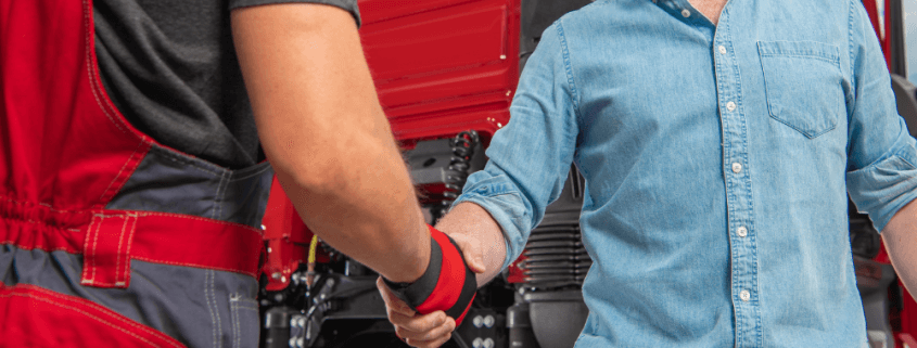 truckers shaking hands in front of red semi-truck